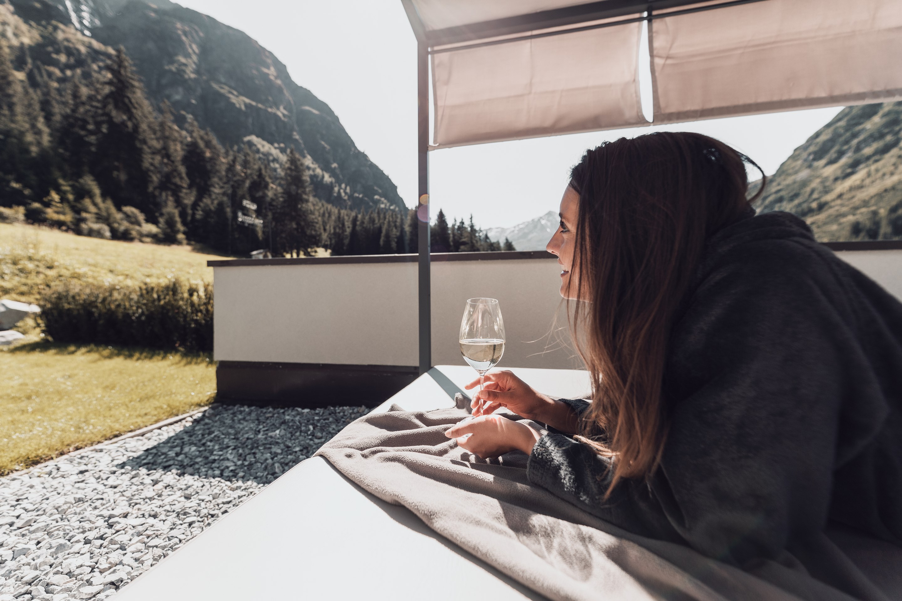Give the gift of joy Woman lying on lounge chair holding a glass of white wine in mountains