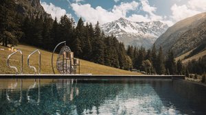 Nicht irgendein Pitztal-Resort: Alpine Resort Sportalm! Berglandschaft mit Schwimmbad und Sitzhocker vor Tannenwald und schneebedecktem Berg